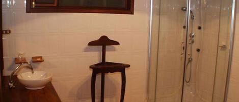 Un baño con lavabo, un taburete de madera y una cabina de ducha de vidrio.