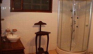 A bathroom with a sink, a wooden stool, and a glass shower enclosure.