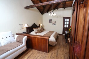 A bedroom with a bed, a wooden headboard, a white sofa, a wooden wardrobe, and a wooden ceiling.