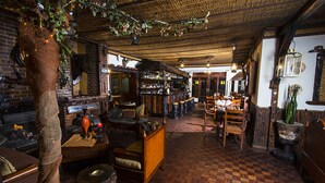 A cozy bar area with wooden furniture, a brick wall, and a thatched ceiling. - Hotel Rumipamba de las Rosas (San Miguel de Salcedo)