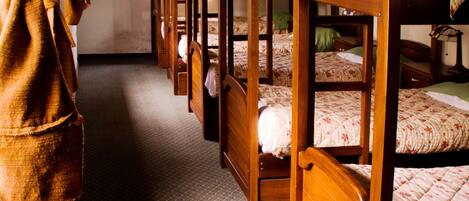 A row of wooden bunk beds in a room with a patterned carpet and a wooden ceiling.