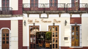A hotel facade with a classic architectural style, featuring a central entrance with double doors, a balcony with wrought iron railings, and a sign above the entrance.