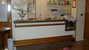 A bar area with a wooden counter, shelves with bottles, and a decorative orchid plant. - Hotel Mayorca (Milan)