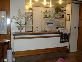 A bar area with a wooden counter, shelves with bottles, and a decorative orchid plant.