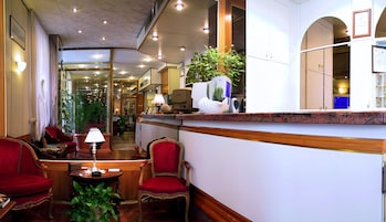 A hotel lobby with a reception desk, red upholstered chairs, a coffee table, and a potted plant.
