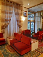 A room with a red sofa, two red armchairs, a small table, and a patterned carpet.