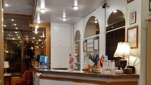 Ein Empfangsbereich mit Theke, Schreibtisch und einem Stuhl. Auf der Theke befinden sich Flaggen, und auf dem Schreibtisch steht eine Lampe.