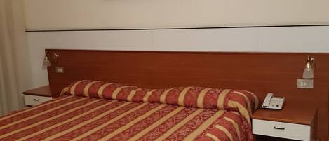 Een hotelkamer met een groot bed, een nachtkastje met een telefoon en een ingelijst foto aan de muur.