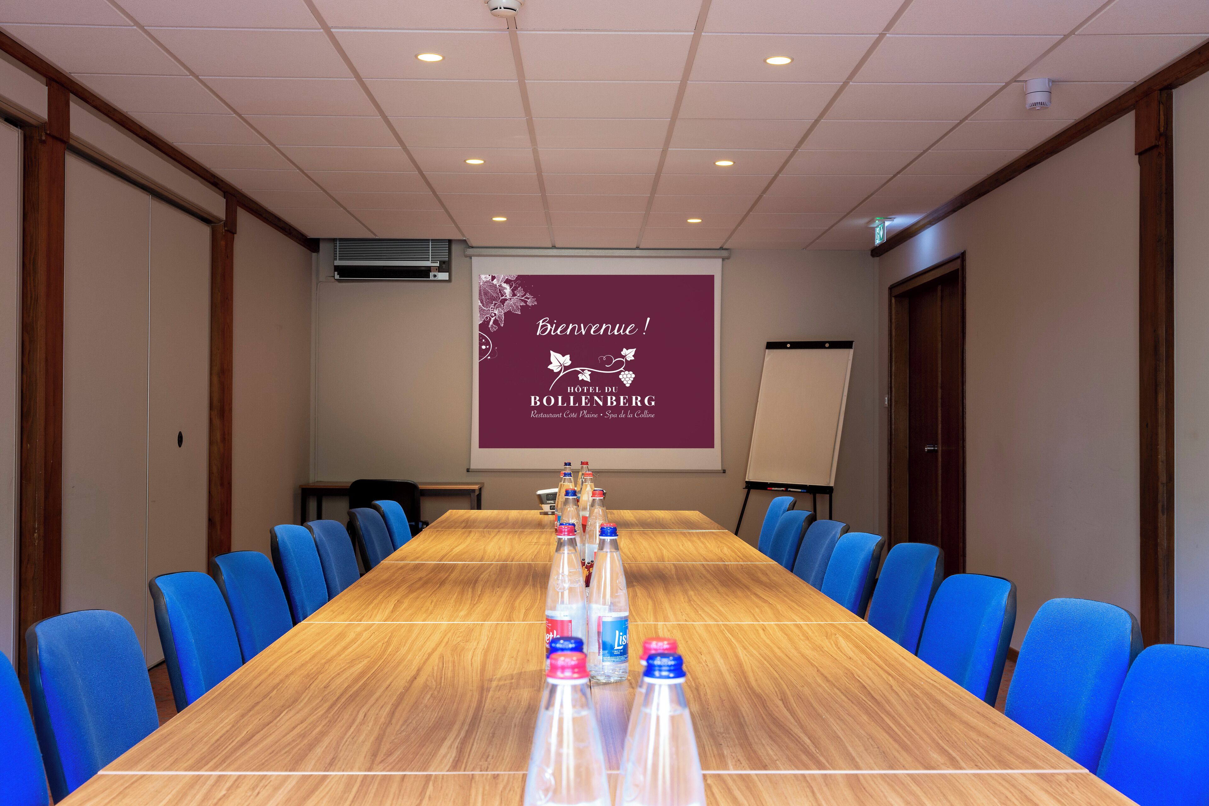A conference room with a long table, blue chairs, and a projector screen displaying a welcome message.