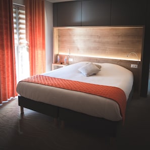 A modern hotel room with a large bed, wooden headboard, bedside tables, and a view of the outdoors.