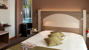 A hotel room with a large bed, a nightstand with a lamp, a chair, a TV, and a wall-mounted waterfall painting. - Hotel du Bollenberg (Westhalten)