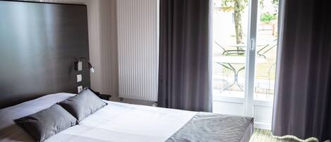 A modern hotel room with a large bed, a wooden ceiling, and a view of the outdoors through a glass door.