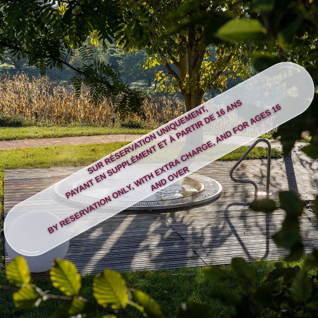 A white sign with red text on a wooden surface, surrounded by greenery.