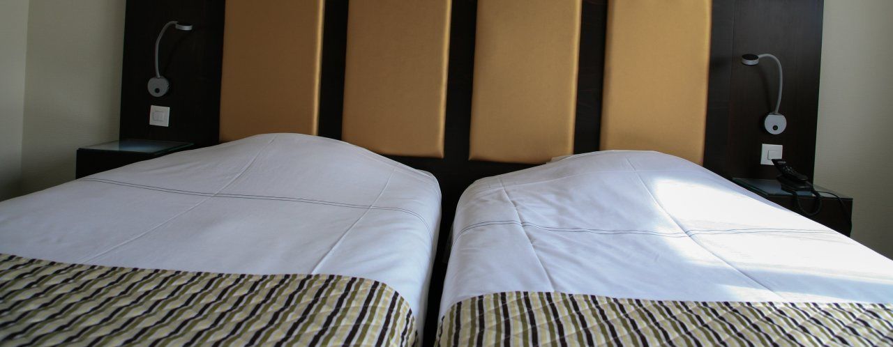 Ett hotellrum med två sängar, en sänggavel med en lampa och ett nattduksbord med en telefon och en laddare.