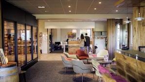 A modern hotel lobby with a reception desk, seating area with colorful chairs, and a wooden accent wall. - Hotel du Bollenberg (Westhalten)