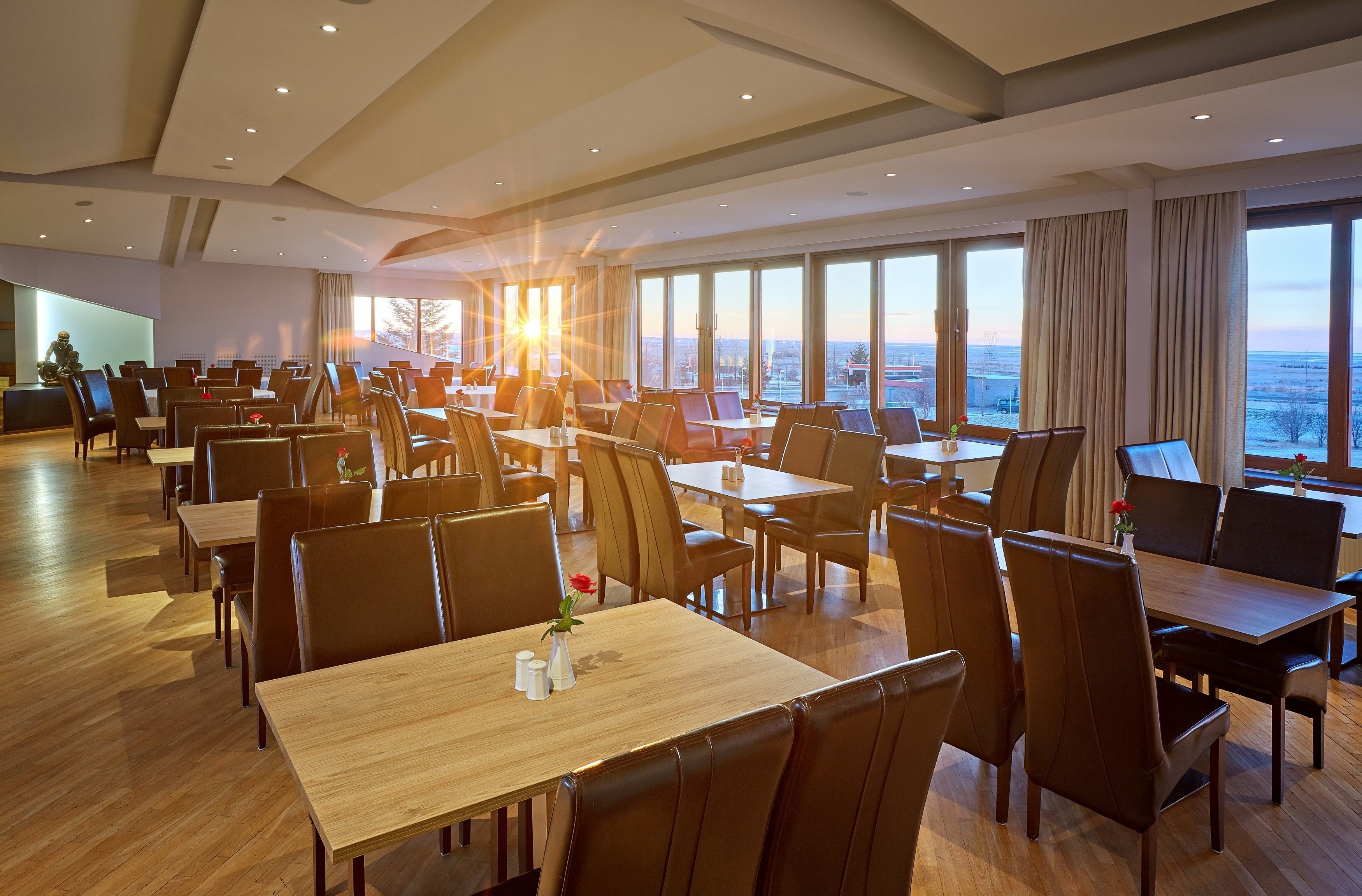 Un comedor amplio con varias mesas y sillas, ventanas grandes que ofrecen vistas a la ciudad y un diseño de interiores moderno.