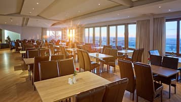 Un comedor amplio con varias mesas y sillas, ventanas grandes que ofrecen vistas a la ciudad y un diseño de interiores moderno.