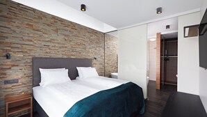 A modern bedroom with a brick-patterned wall, a large bed with white bedding, a bedside table, and a dark wooden bench. - Hotel Örk (Hveragerdi)