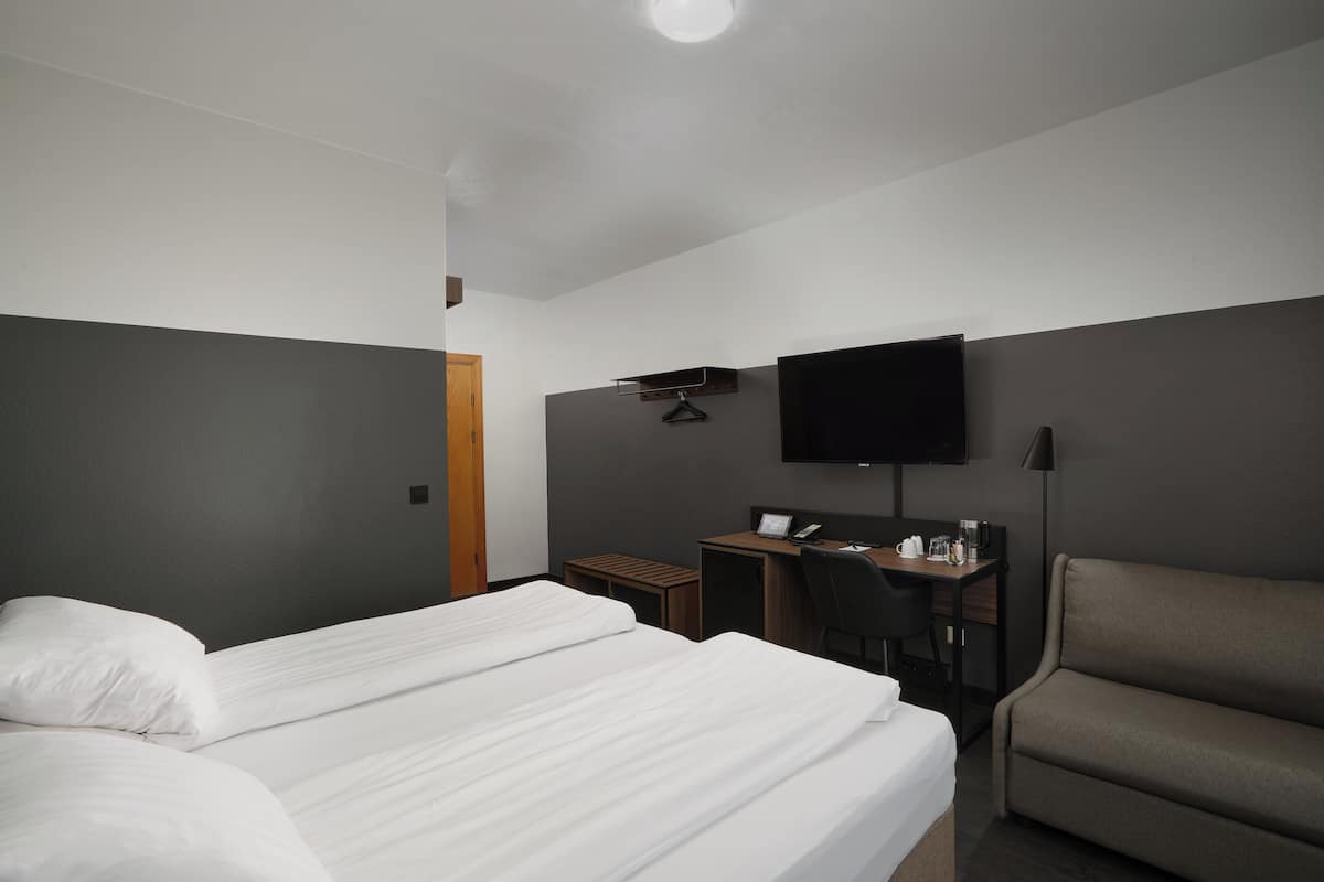 A hotel room with a bed, a desk, a chair, a TV, and a sofa.