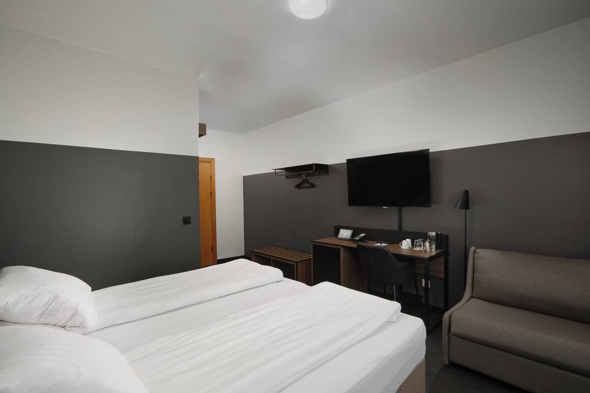 Una habitación de hotel con cama, escritorio, silla, televisor y sofá.