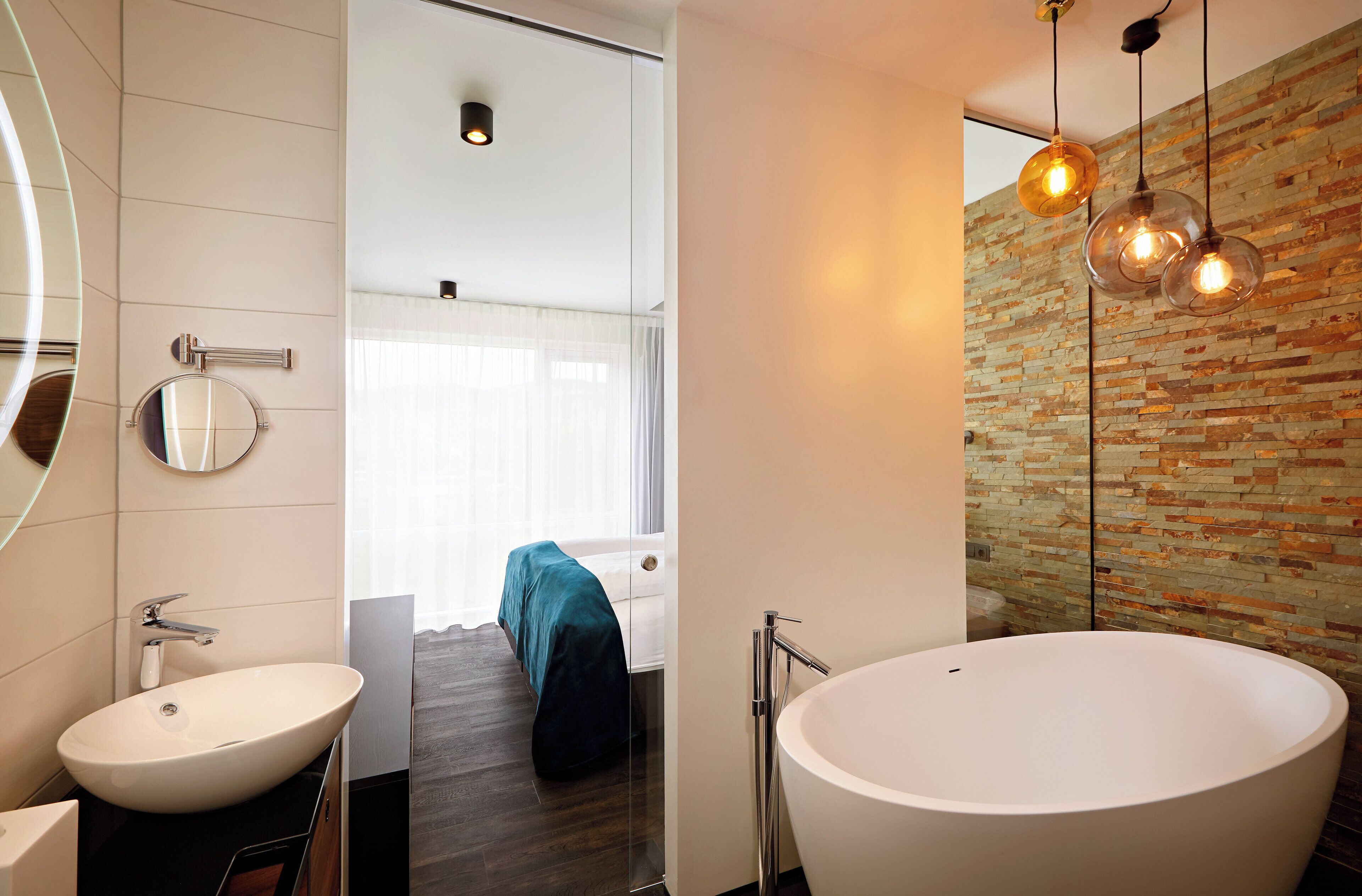 A modern bathroom with a large white bathtub, a round mirror, and a sleek vanity.