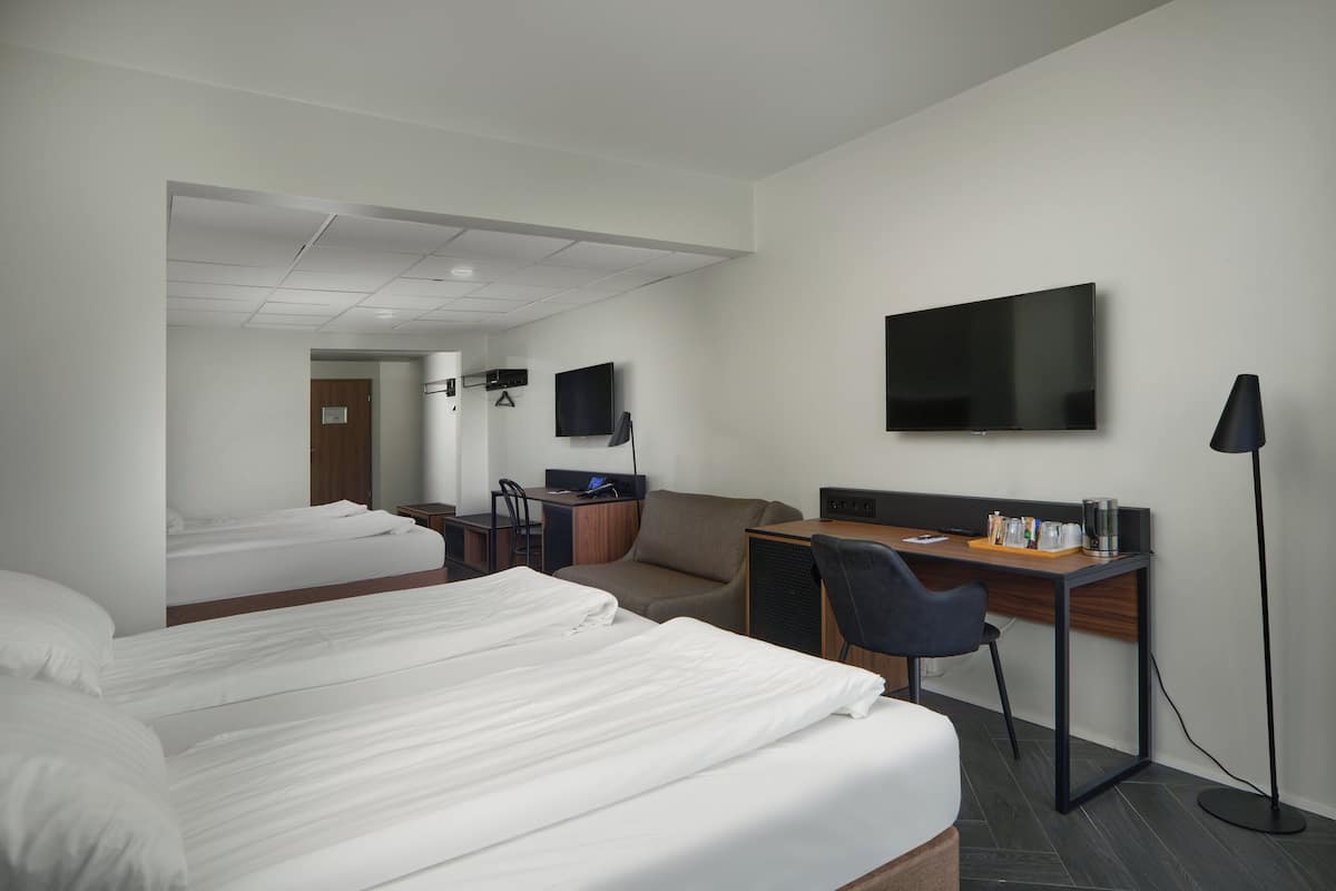 A hotel room with two beds, a desk, a chair, a television, and a floor lamp.