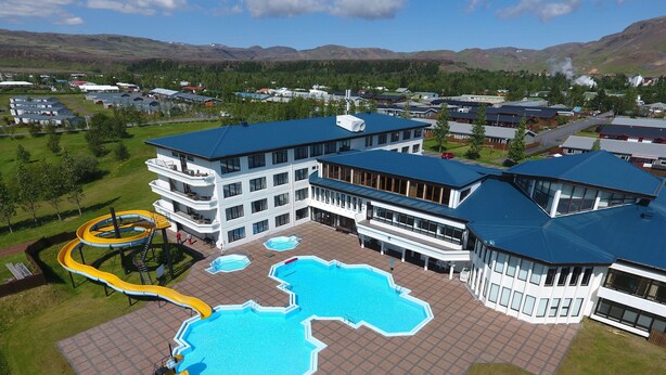 A hotel with multiple swimming pools, a water slide, and a large umbrella. - Hotel Örk (Hveragerdi)