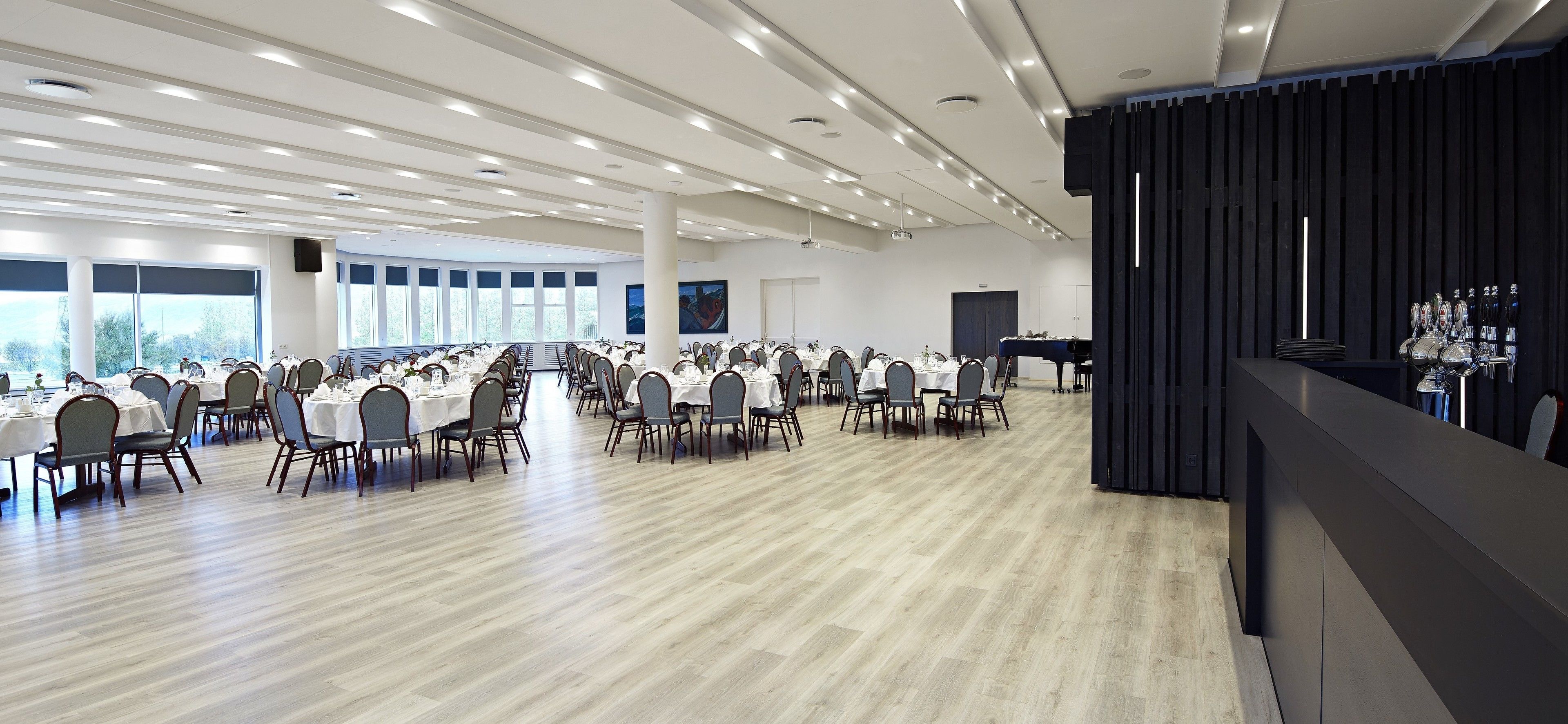 A spacious conference room with rows of tables and chairs, large windows, and a piano.