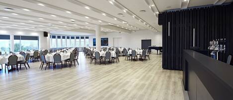A spacious conference room with rows of tables and chairs, large windows, and a piano.