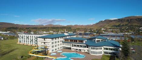 Un hotel con piscina, zona de juegos para niños y vistas a montañas.