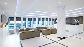 A modern hotel lobby with a reception desk, seating area, and large windows offering city views. - Hotel Örk (Hveragerdi)