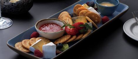A rectangular serving tray with various cheeses, crackers, and berries, accompanied by small bowls of dips.