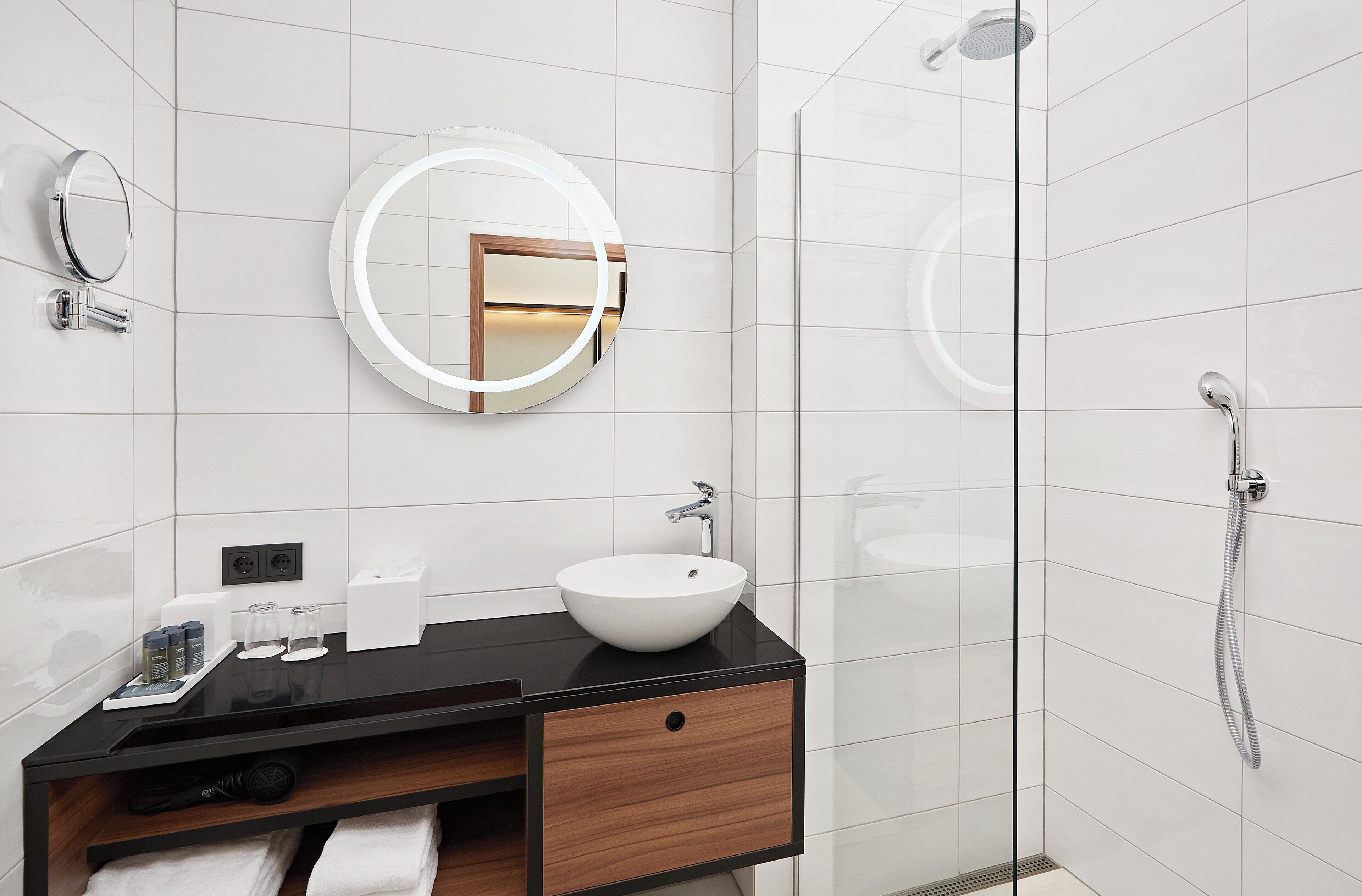 Une salle de bain moderne avec un plan de toilette noir, un lavabo blanc et une douche à parois de verre.