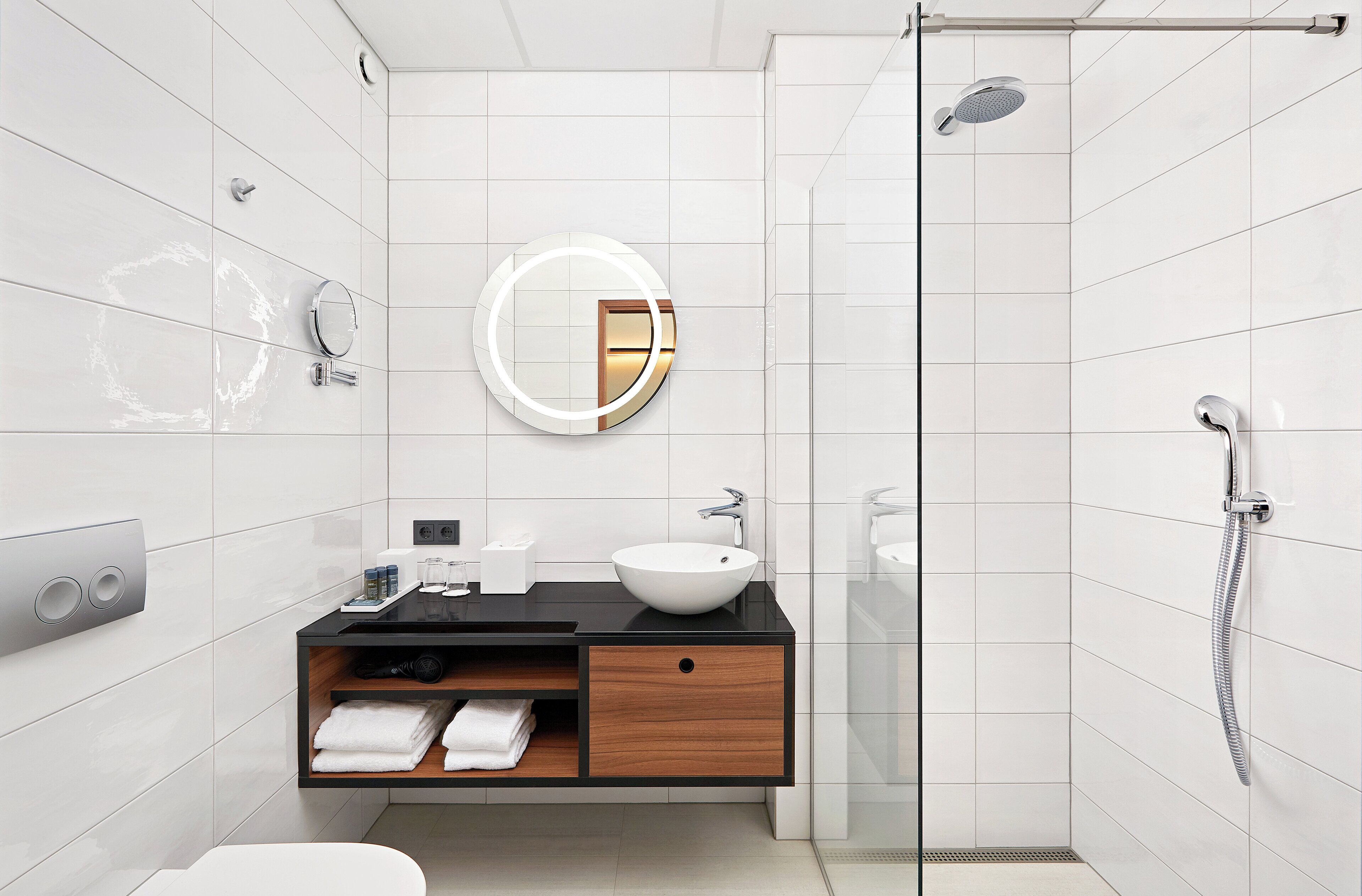 Un baño moderno con un lavamanos blanco, un espejo redondo y una zona de ducha.
