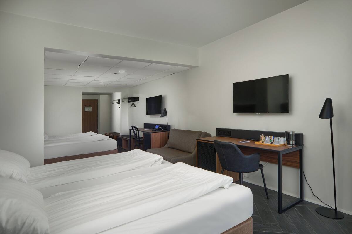 Una habitación de hotel con dos camas, un escritorio, una silla, un televisor y una lámpara de pie.