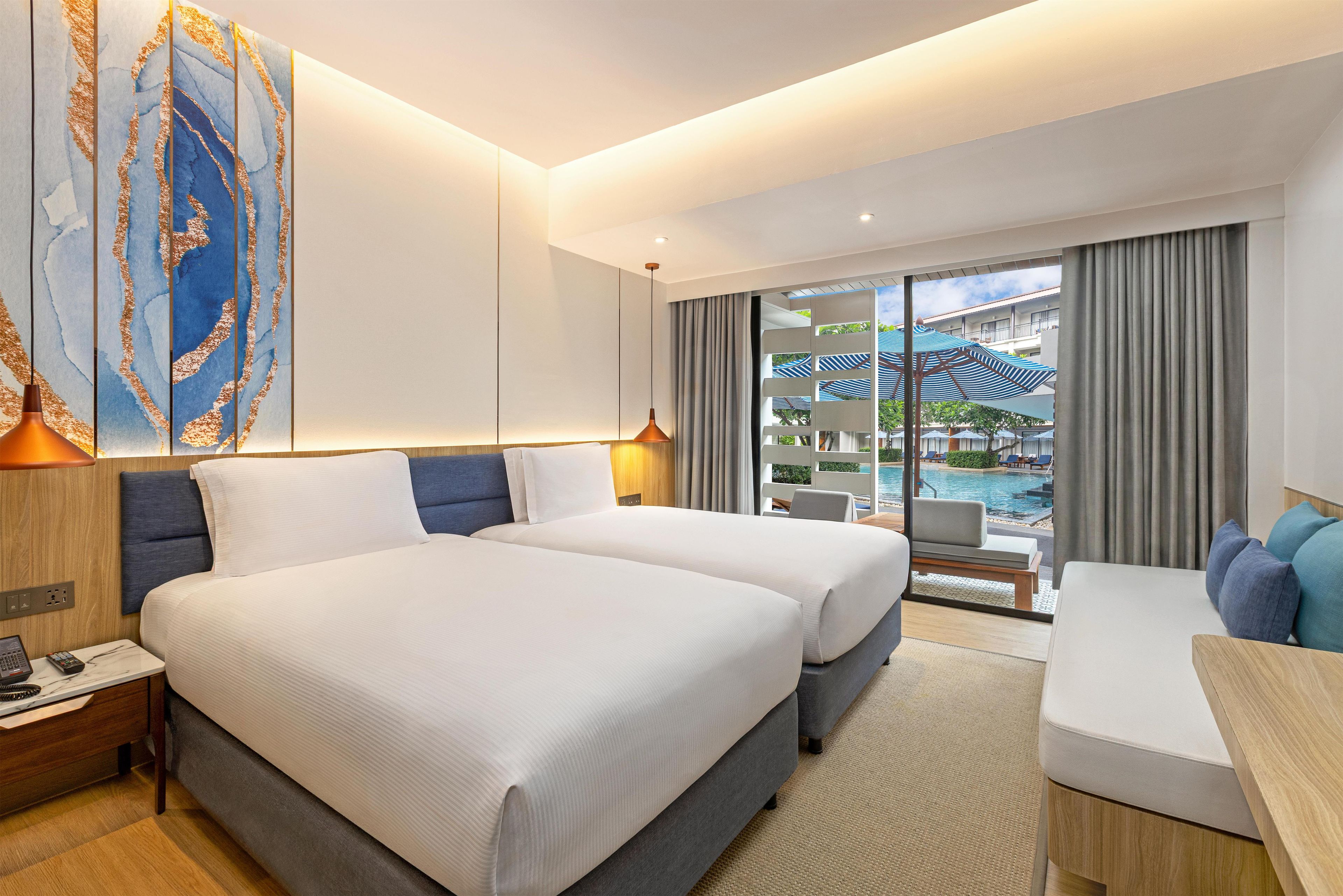 Quarto de hotel com duas camas, uma mesa de trabalho, uma cadeira e vista para a piscina e área externa.