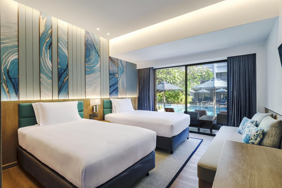 Habitación de hotel con dos camas, un sofá, un ventanal con vistas a una piscina y un panel decorativo en la pared.