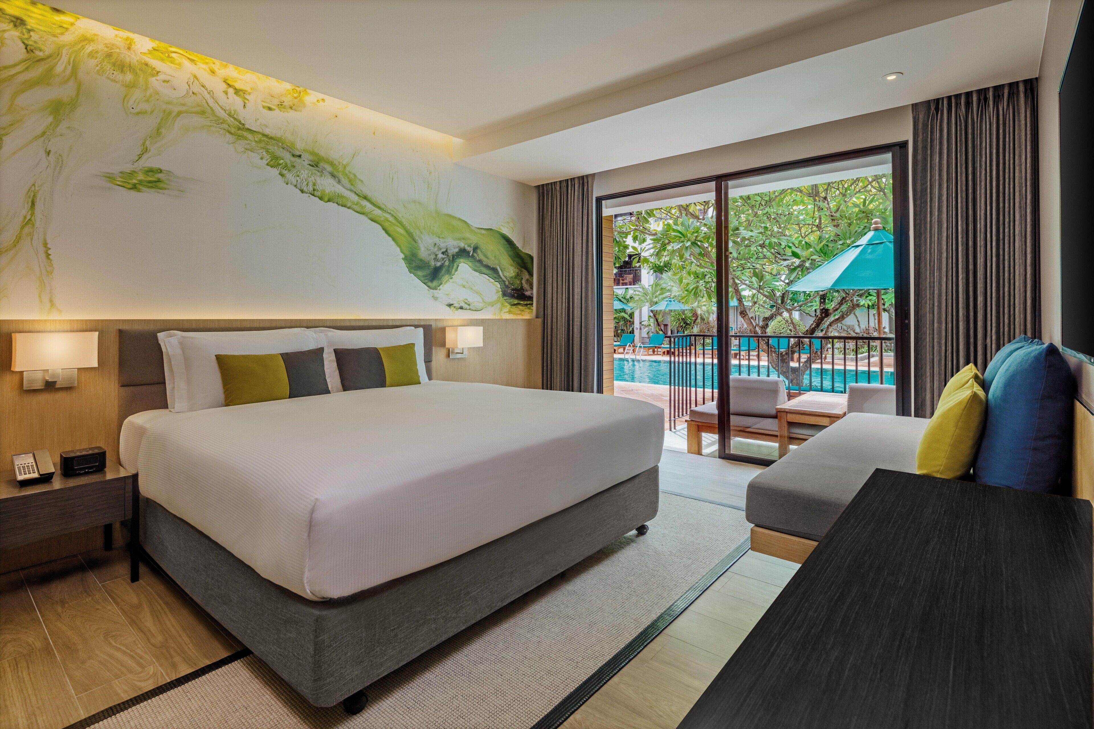 Una habitación de hotel moderna con una cama grande, un sofá, un escritorio y un balcón con vista a la piscina.