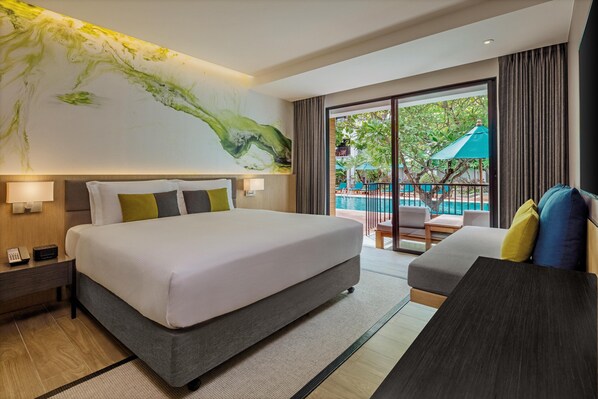 A modern hotel room with a large bed, a sofa, a desk, and a balcony with a pool view.