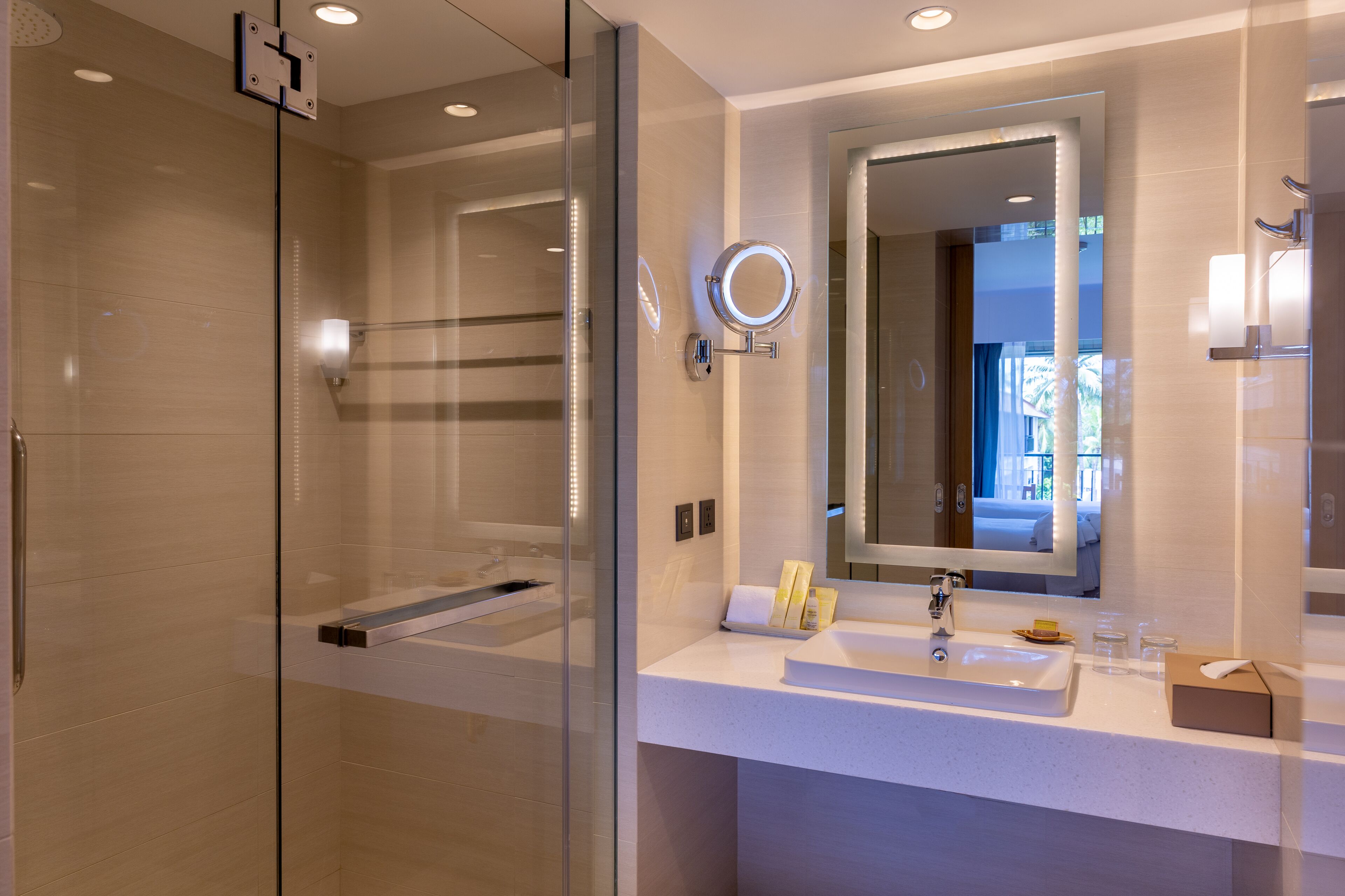 A modern bathroom with a glass-enclosed shower, a large mirror, and a white sink with toiletries.