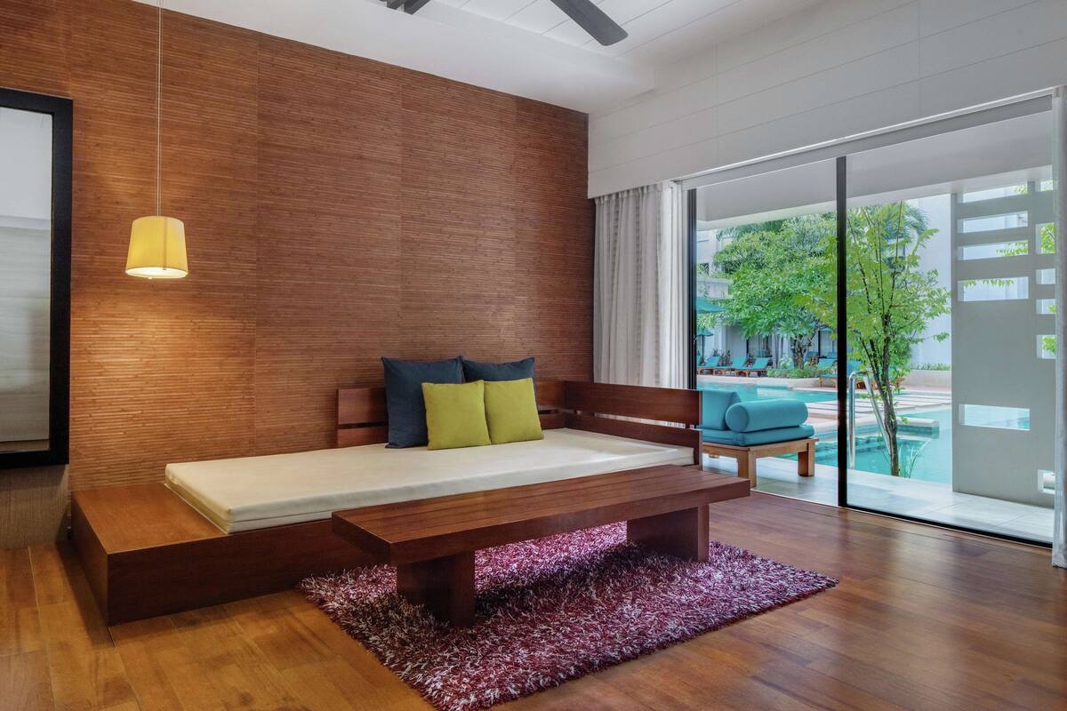 Un dormitorio moderno con una cama de madera estilo banco, una lámpara colgante y vistas a una zona de piscina al aire libre.