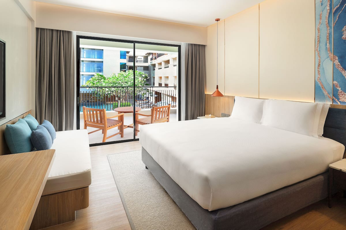 Habitación de hotel con una cama grande, un escritorio, una silla y un balcón con vista a la ciudad.