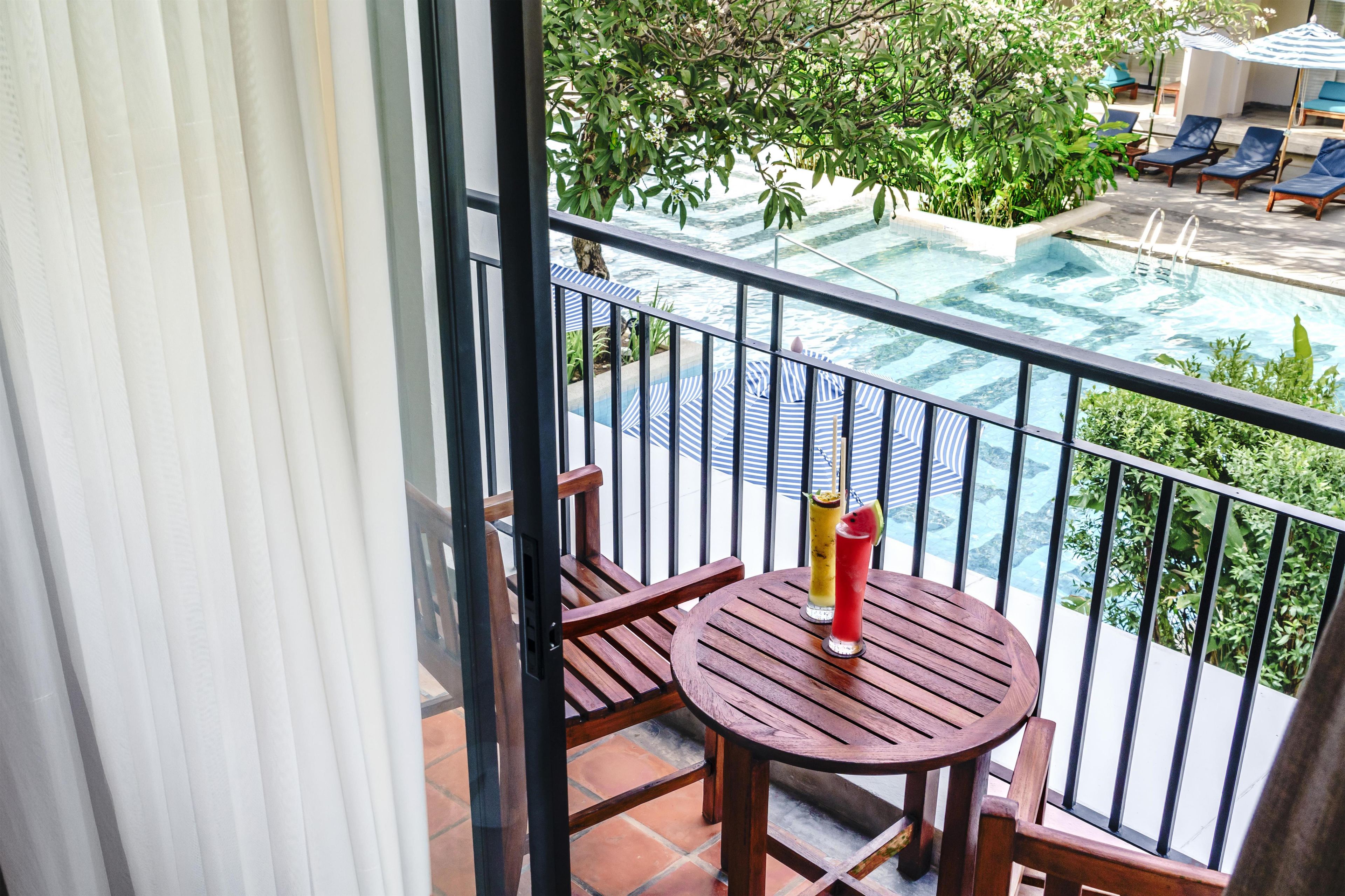 Un balcón con vista a una piscina, dos sillas y una mesa con una bebida.