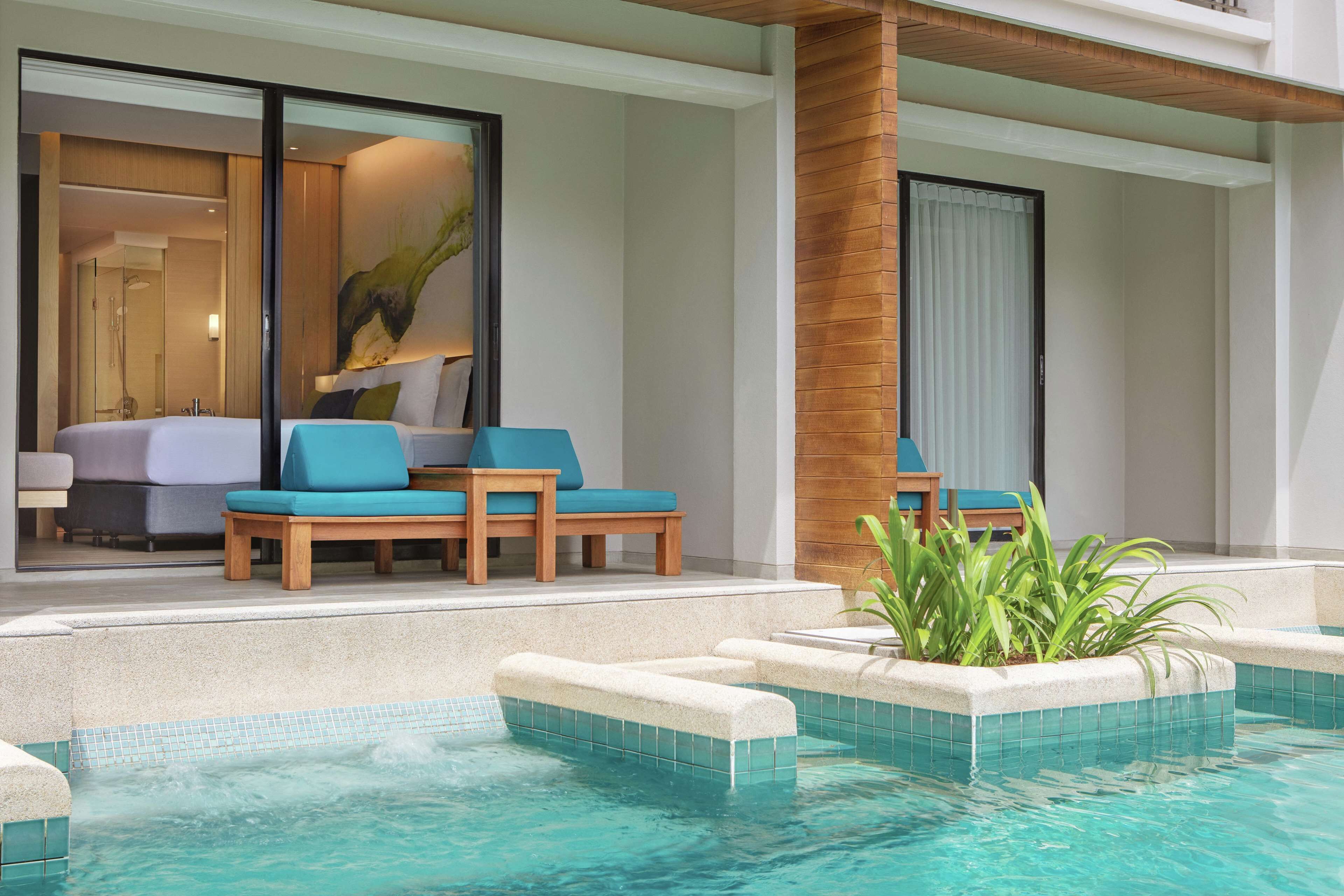 Une chambre d’hôtel moderne dotée d’une grande fenêtre, d’un coin salon avec un canapé et des fauteuils, et d’un espace piscine avec un jacuzzi.