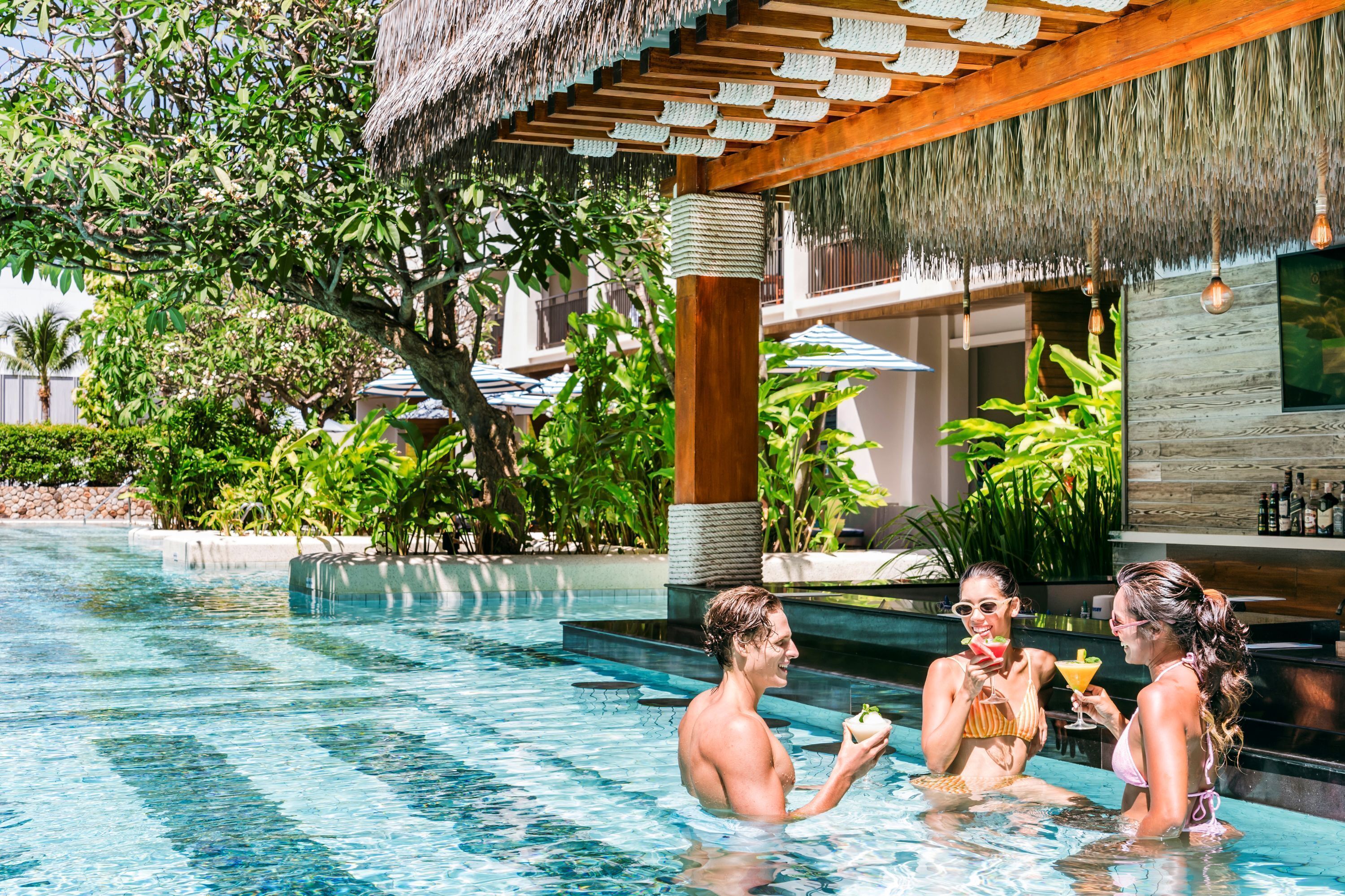 A pool area with a thatched roof, surrounded by lush greenery and a bar area with a wooden interior.