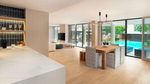 A modern kitchen with a marble countertop, a dining area with a wooden table and patterned chairs, and large sliding glass doors leading to a pool area.