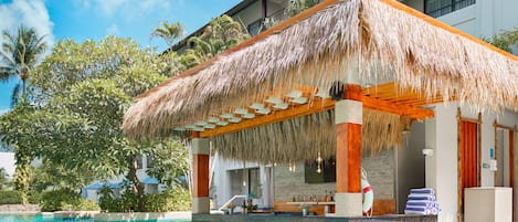 A poolside area with a thatched roof structure, a bar, and a lifebuoy.