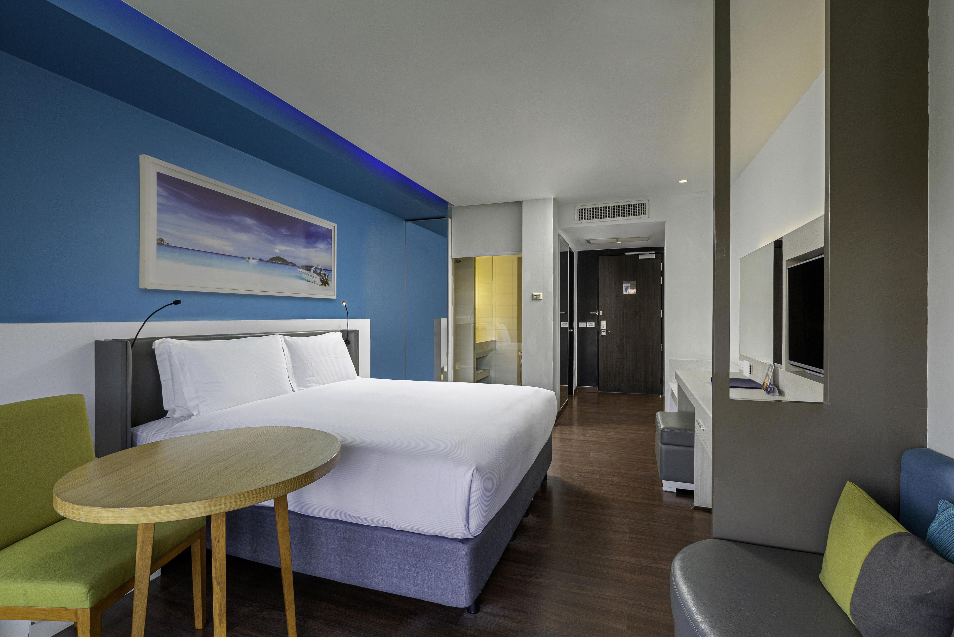 Een hotelkamer met een bed, een tafeltje, een stoel, een televisie en een schilderij aan de muur.