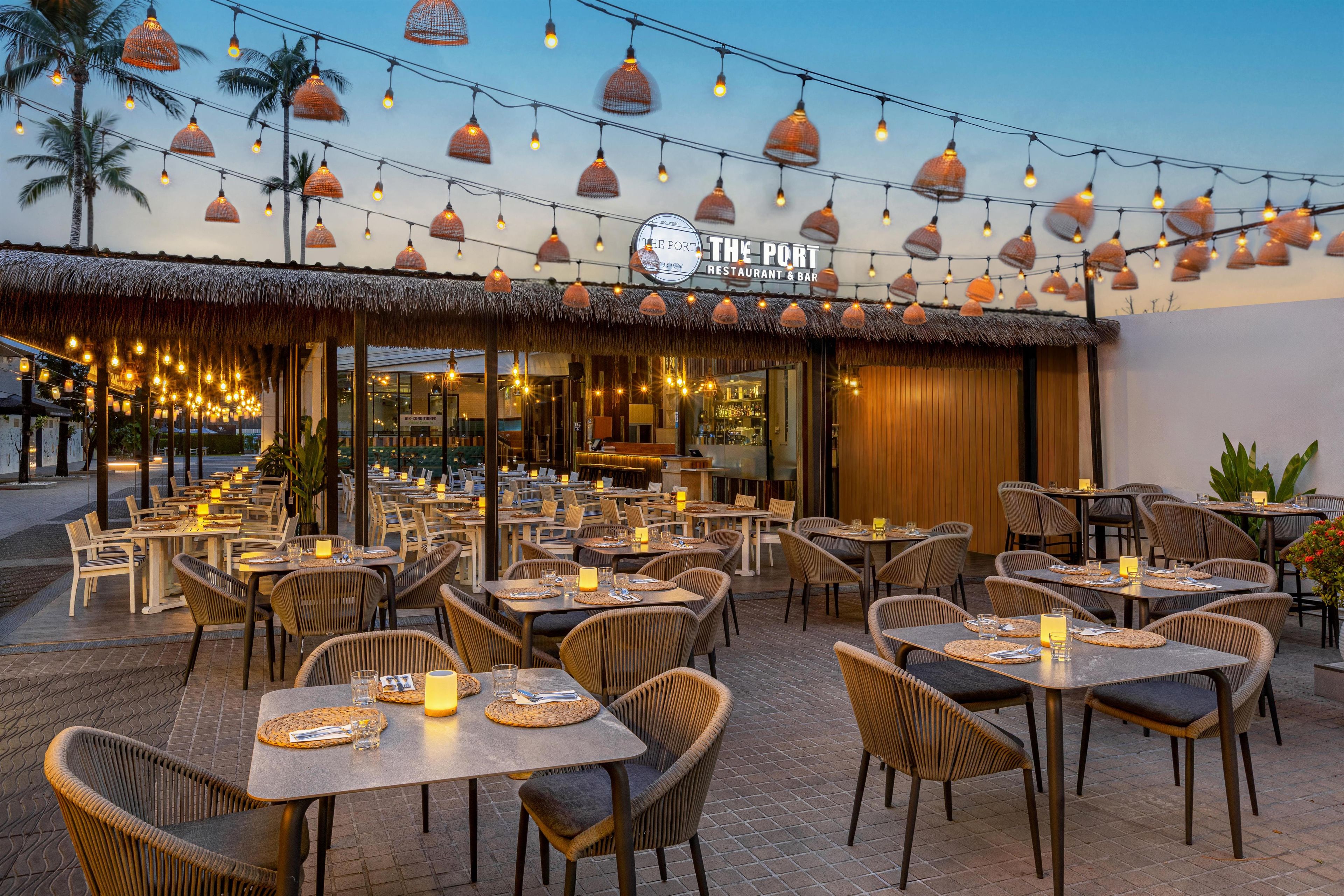 An outdoor dining area with tables and chairs, string lights, and a restaurant sign.