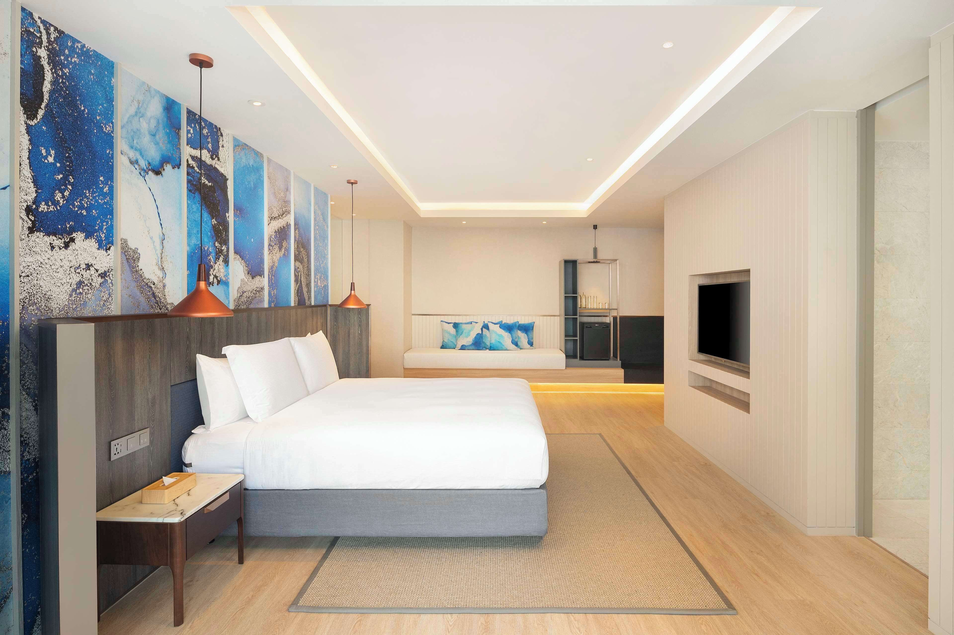 A modern hotel room with a large bed, a bedside table, a TV, and a wall with abstract art.